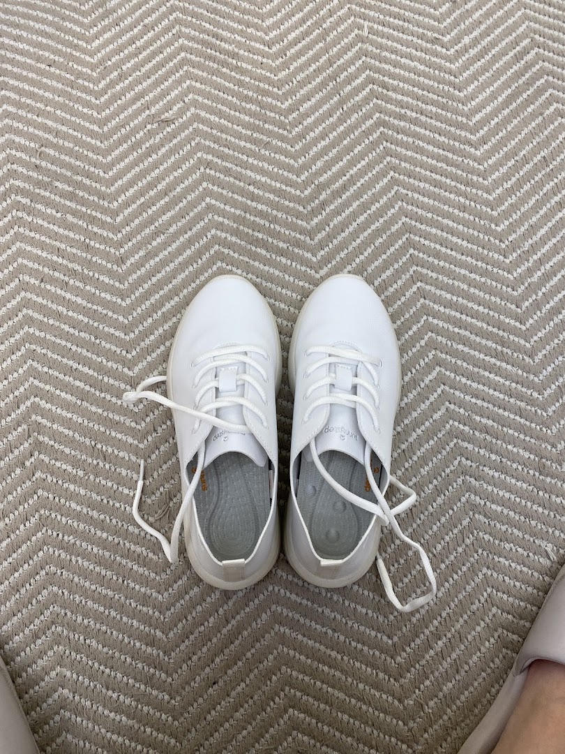 A pair of white Sunnystep sneakers on a patterned carpet, showcasing the brand's footwear.
