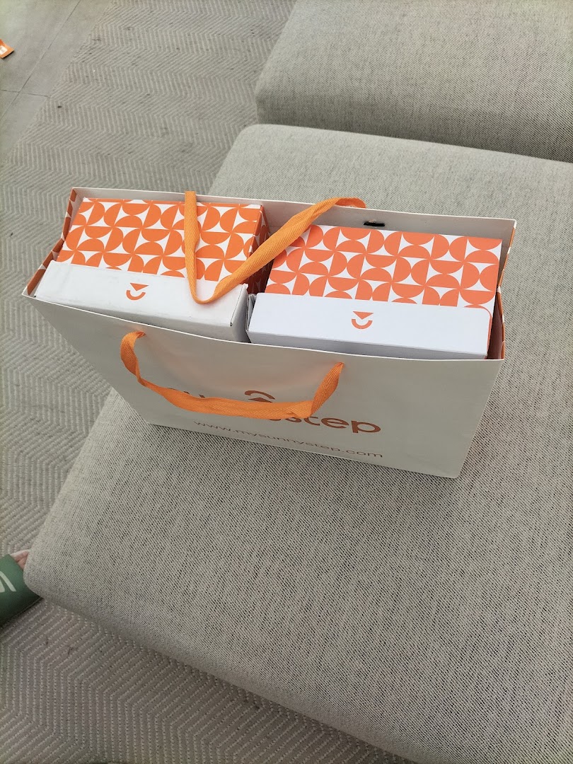 A white Sunnystep shopping bag containing two orange-patterned product boxes, resting on a sofa.