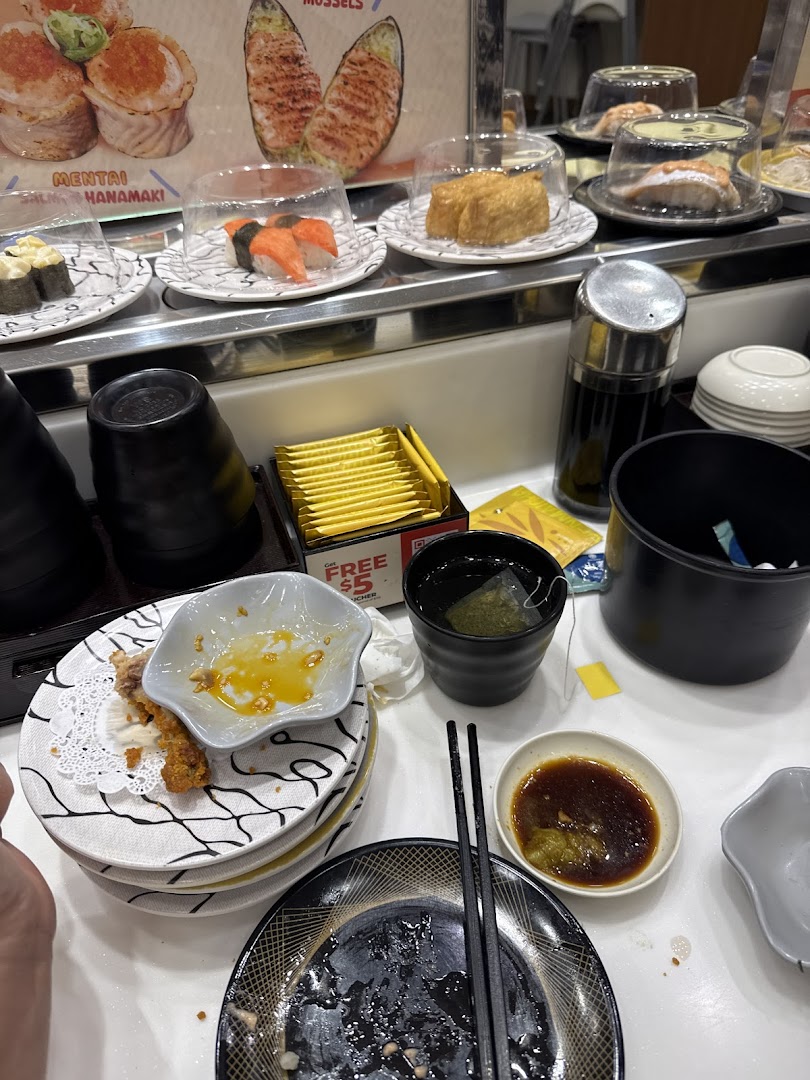 A bustling sushi conveyor belt restaurant with various sushi plates, condiments, and used dishes on the table.