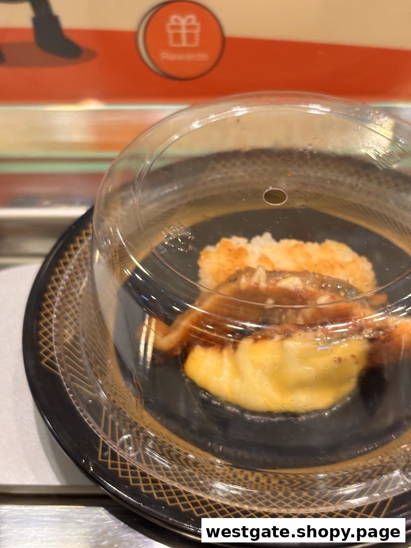 A covered sushi plate with eel and tamago on a conveyor belt at Sushi Express.
