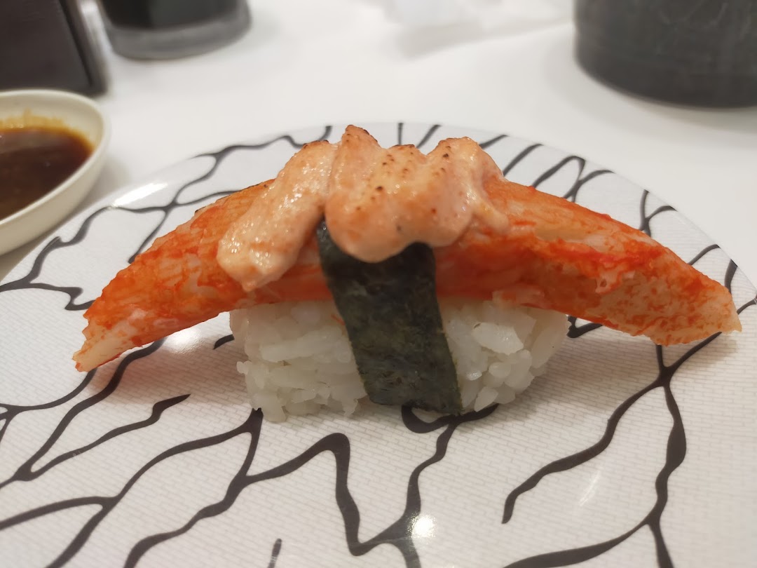 A close-up of a delicious crab stick sushi topped with creamy sauce on a patterned plate.