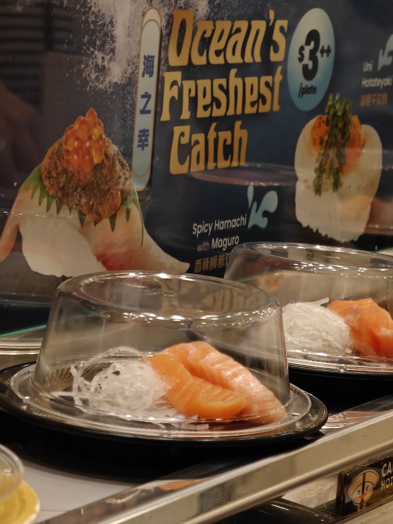 Fresh sushi plates, including salmon, on a conveyor belt with a promotional sign for 'Ocean's Freshest Catch'.