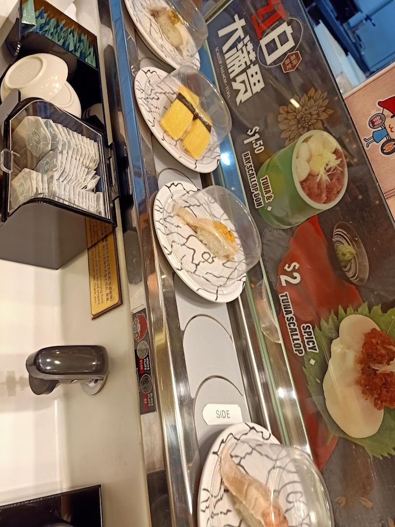 A vibrant view of a sushi conveyor belt with various covered plates and a promotional display.