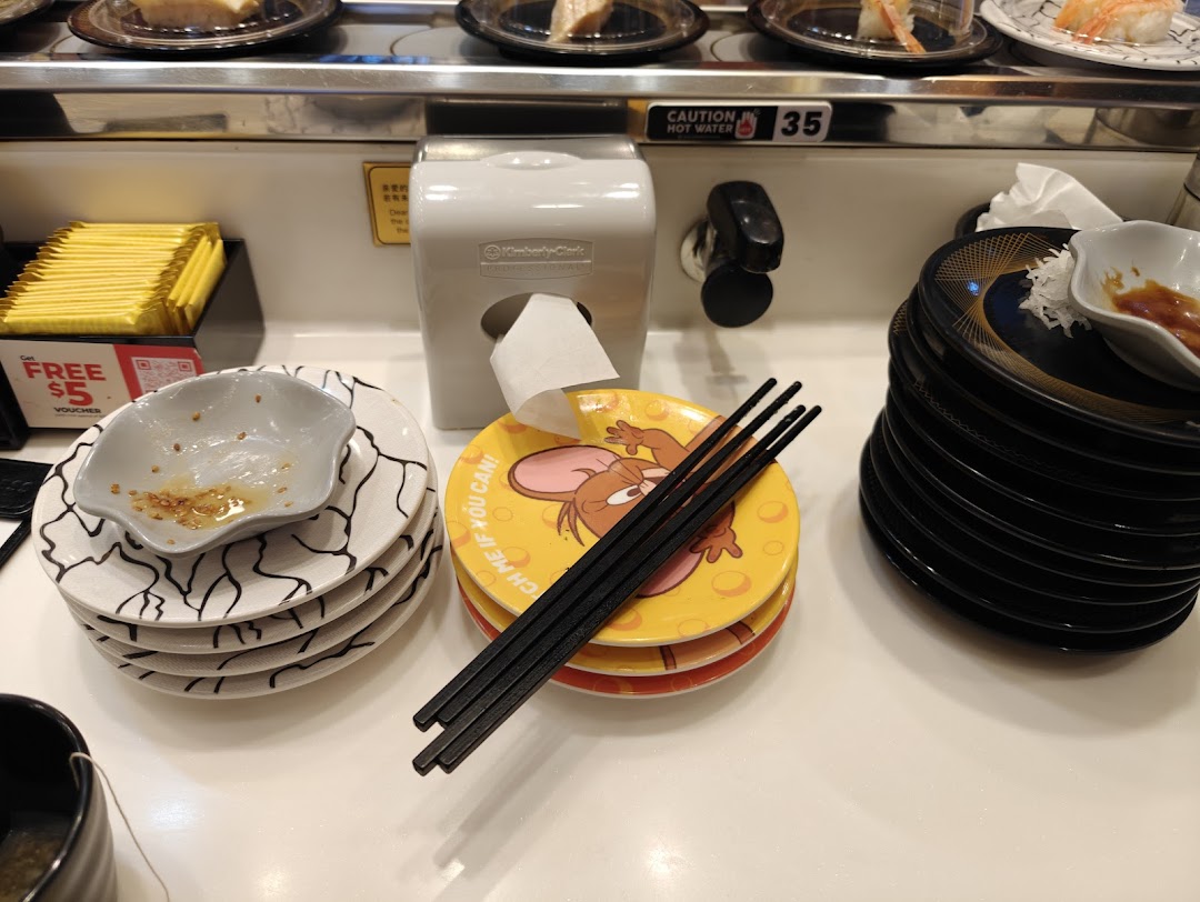 A close-up of a sushi conveyor belt dining area with plates, chopsticks, and a hot water tap.