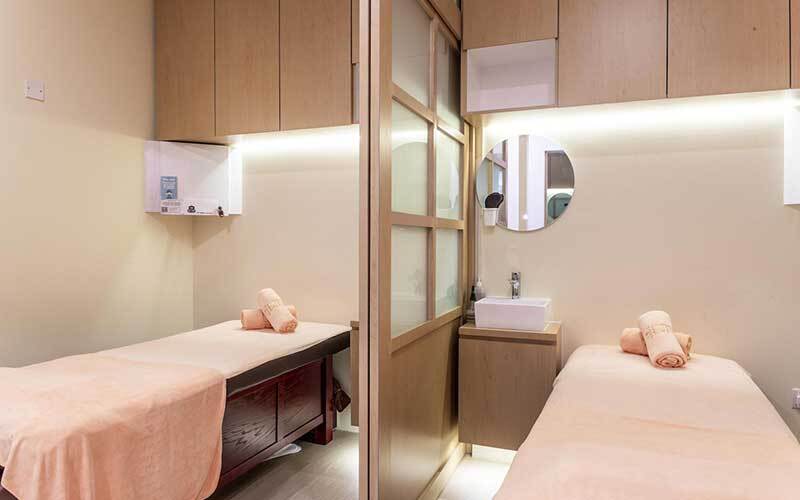 Two treatment beds in a clean, modern spa room with wooden accents and soft lighting.
