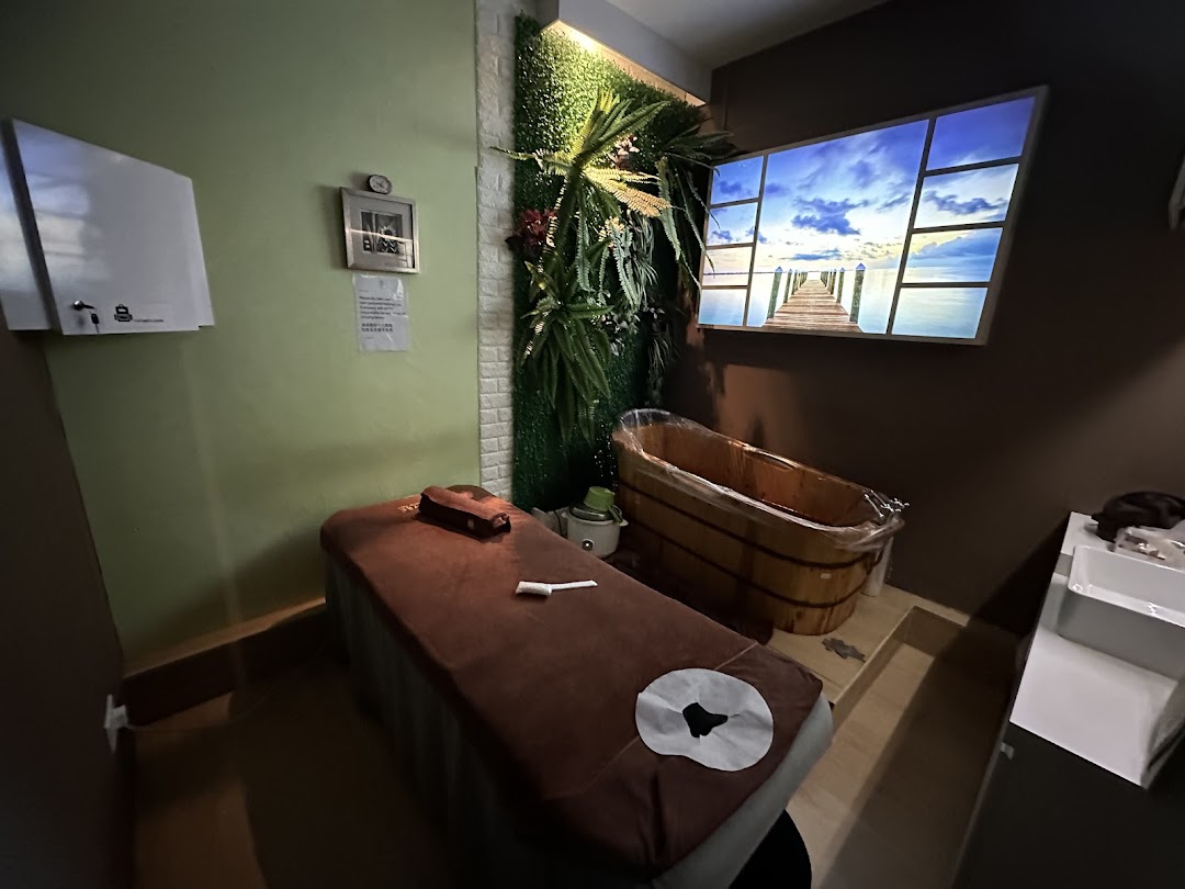 A serene spa treatment room featuring a massage bed, wooden tub, and scenic wall display.