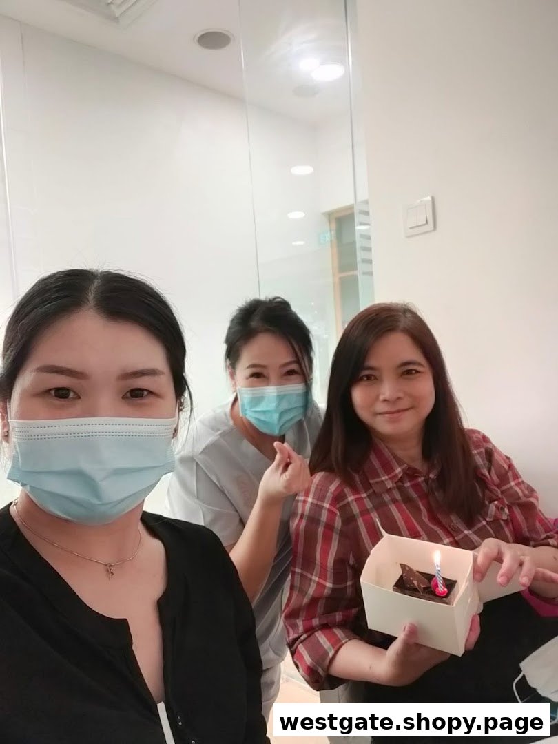 Three staff members celebrating with a small cake and candle in a bright, clean interior.