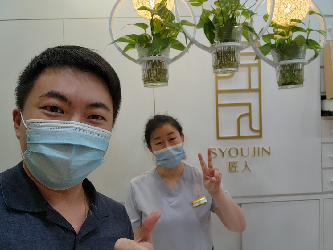 Two masked individuals pose inside Syoujin, featuring its logo and decorative hanging plants.