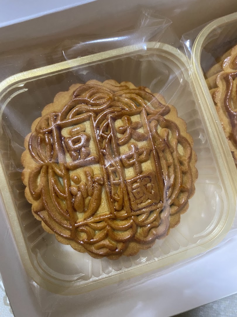 A close-up of a traditional mooncake with intricate patterns, packaged in a clear plastic tray.