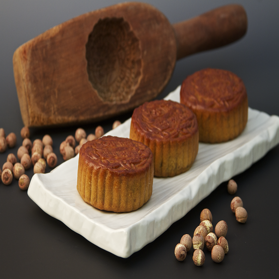 Three golden mooncakes on a white platter with lotus seeds and a traditional mold.