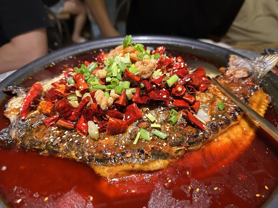 A vibrant, spicy whole fish dish, generously topped with chilies, green onions, and crispy bits in a rich red sauce.