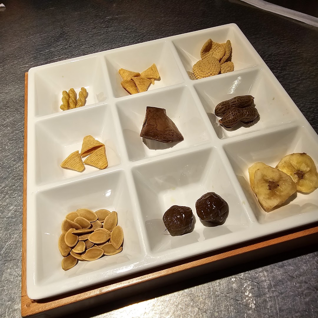 A white nine-compartment tray filled with various snacks like nuts, dried fruits, and crispy bites.