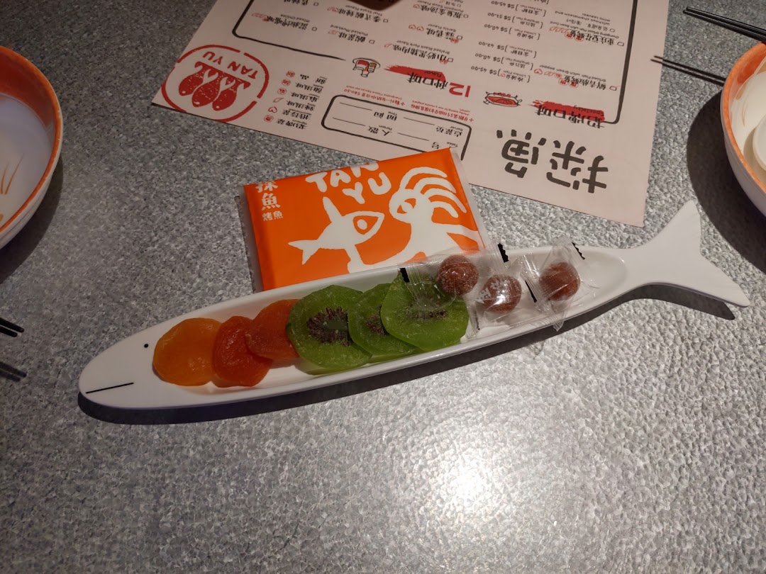 A table setting at TANYU featuring a fish-shaped dish with dried fruits, an orange box, and a menu.