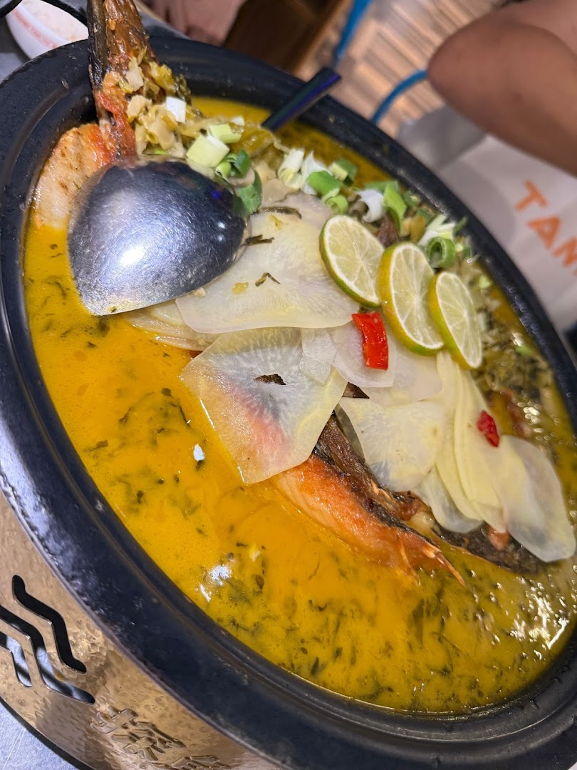 A vibrant close-up of TANYU's signature grilled fish in a rich golden broth, garnished with lime and vegetables.