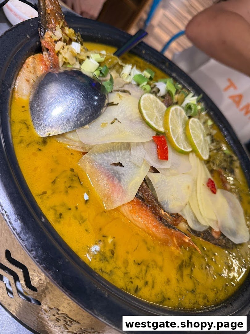 A vibrant close-up of TANYU's signature grilled fish in a rich golden broth, garnished with lime and vegetables.