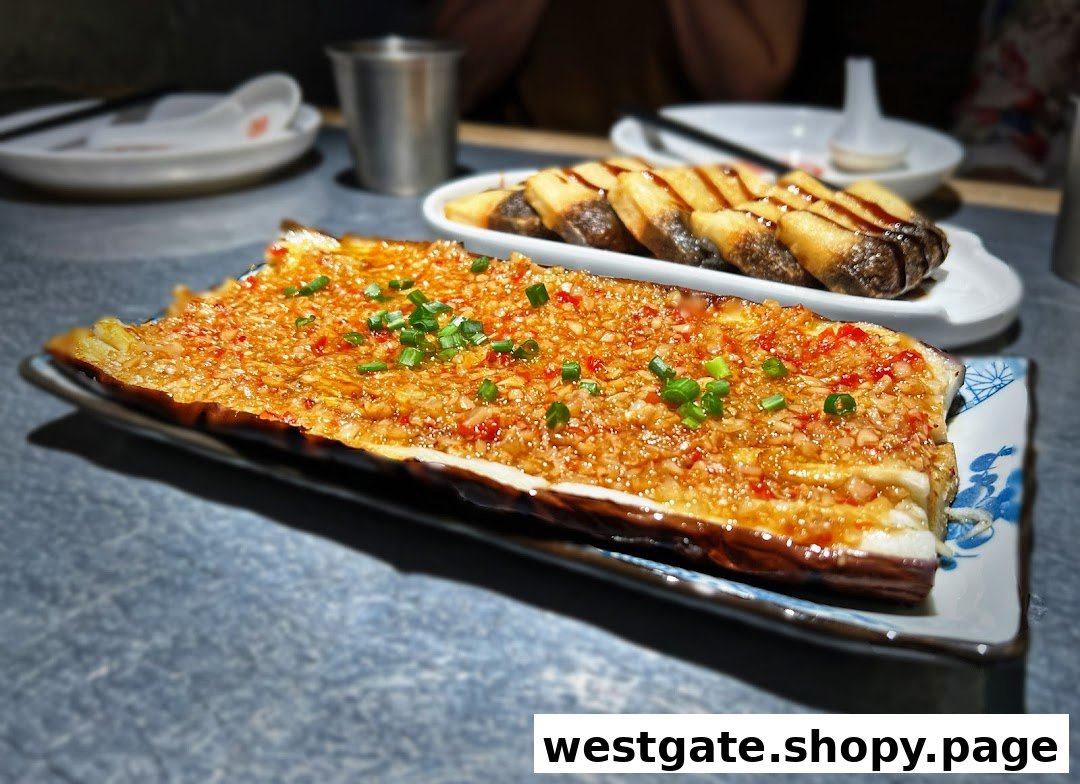 A close-up of grilled eggplant with garlic and chili, alongside another dish on a table.