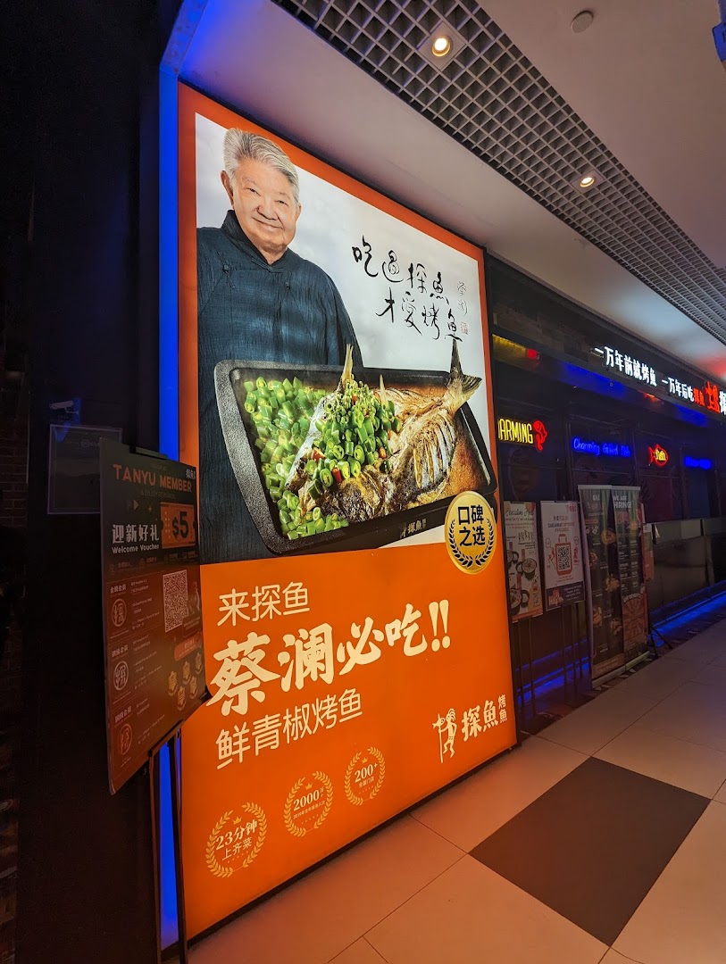 A large illuminated sign for TANYU featuring a man and a roasted fish dish, positioned at the shop's entrance.