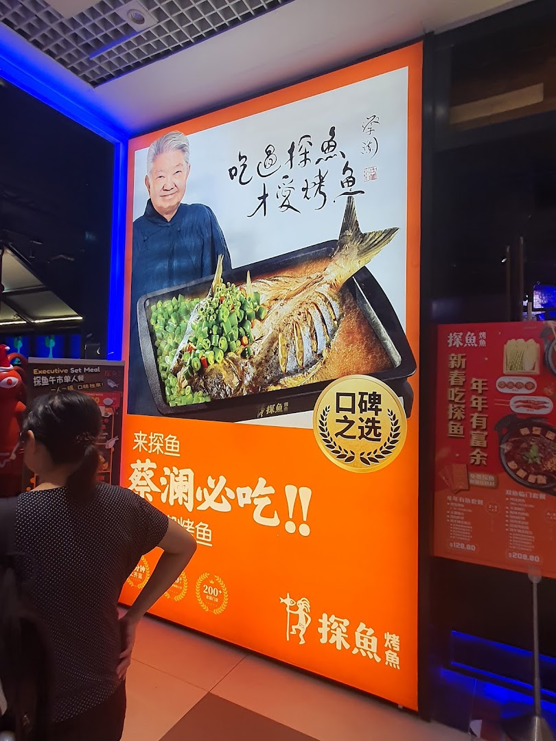 A large, vibrant orange promotional display for TANYU featuring a roasted fish dish, an elderly man, and Chinese text.