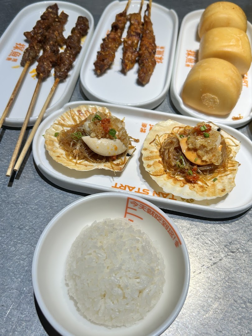A close-up of various delicious dishes from TANYU, including grilled skewers, baked scallops, steamed buns, and white rice.