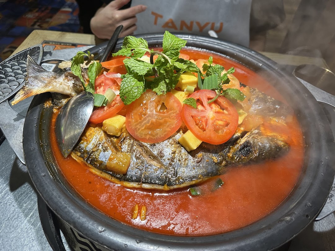A vibrant roasted fish dish in a rich red sauce, garnished with fresh tomatoes and mint, served steaming hot at TANYU.