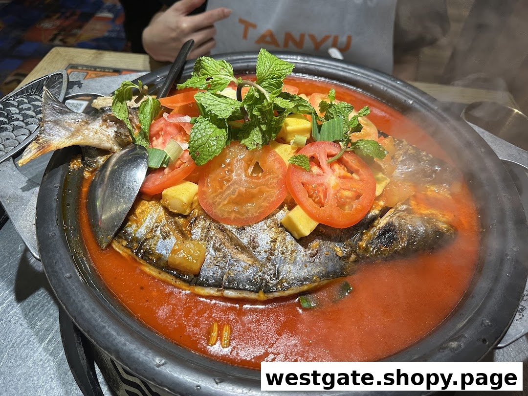 A vibrant roasted fish dish in a rich red sauce, garnished with fresh tomatoes and mint, served steaming hot at TANYU.