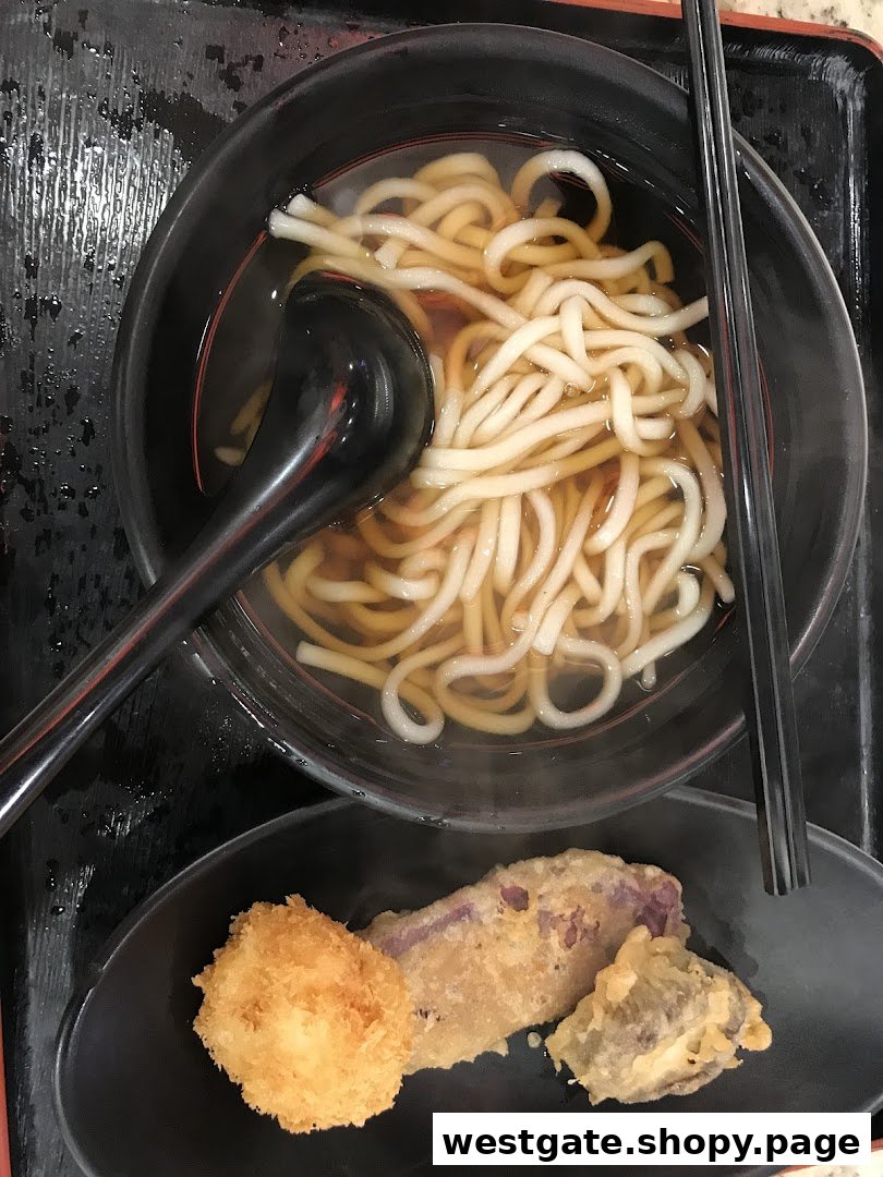 A close-up of a comforting bowl of udon noodles served with a side of crispy tempura.