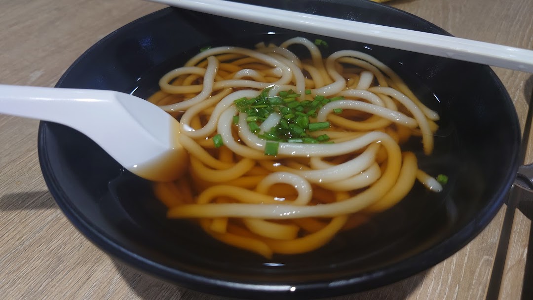 A close-up of a bowl of hot udon noodles in broth, garnished with chopped chives.