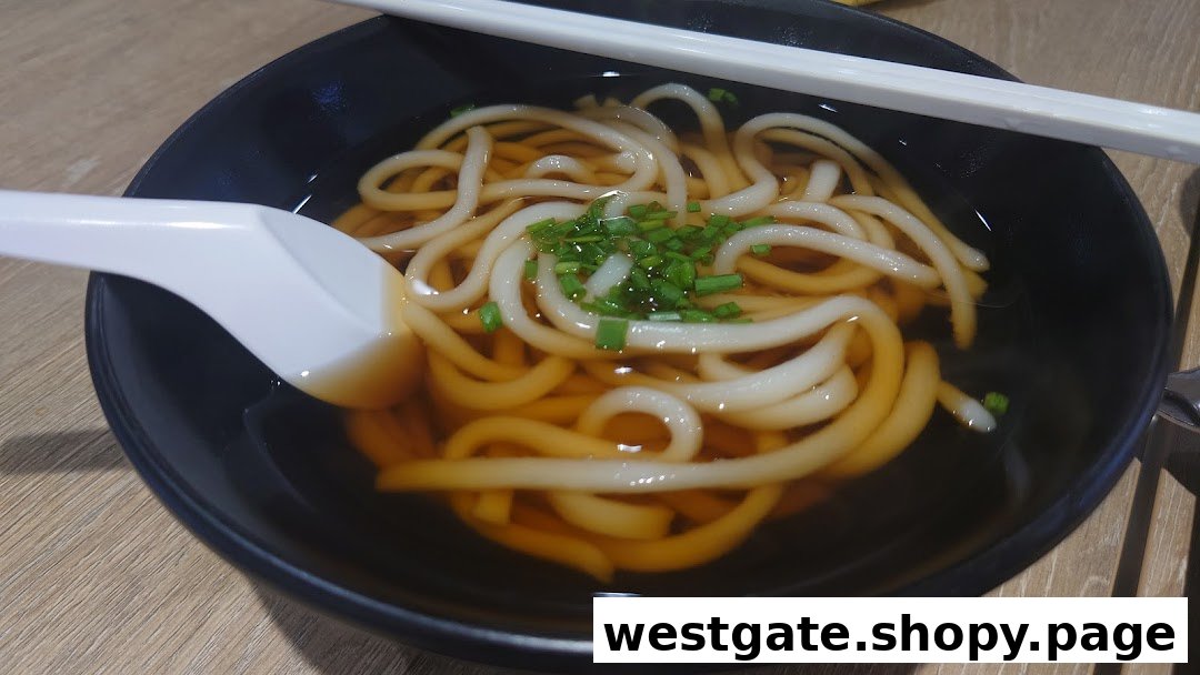 A close-up of a bowl of hot udon noodles in broth, garnished with chopped chives.