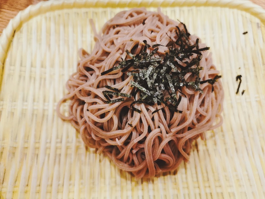 A close-up of soba noodles topped with shredded nori, served on a traditional bamboo mat.