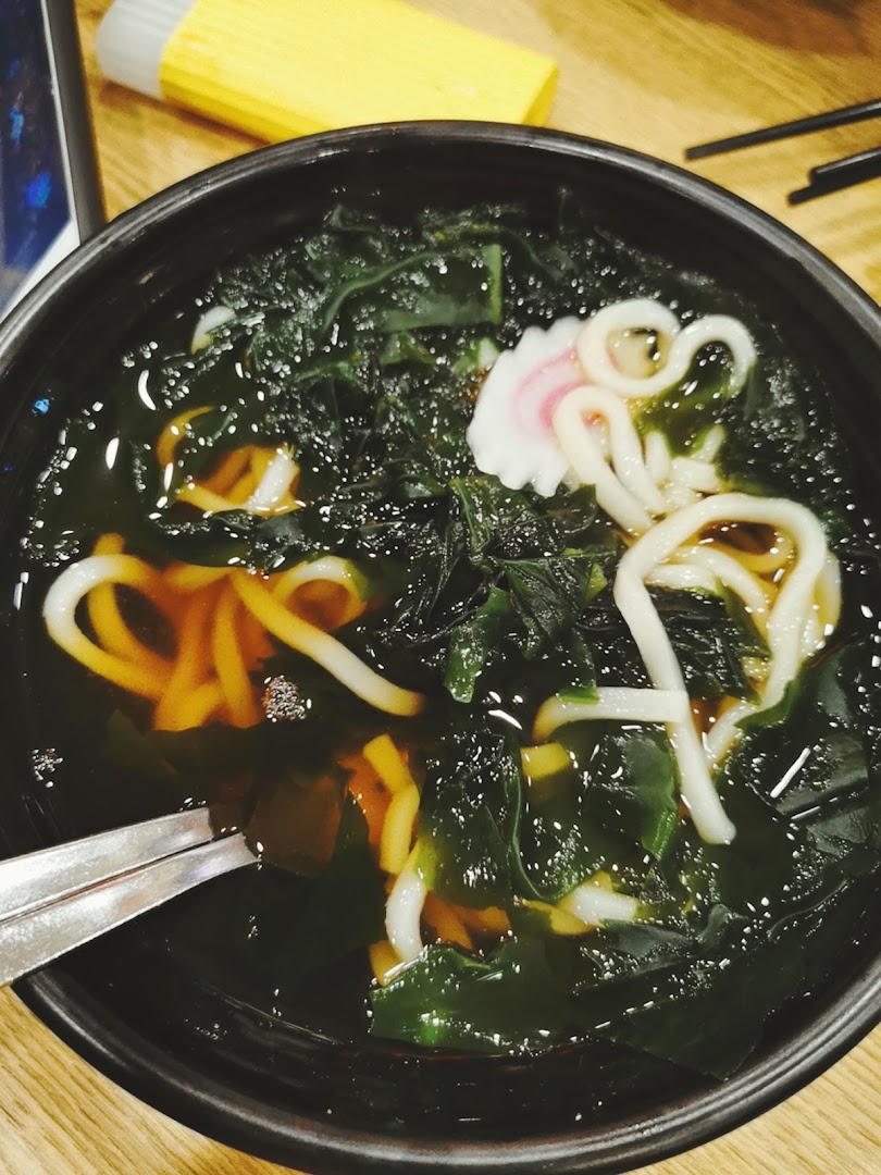 A close-up of a delicious bowl of udon noodles with seaweed and narutomaki fish cake.