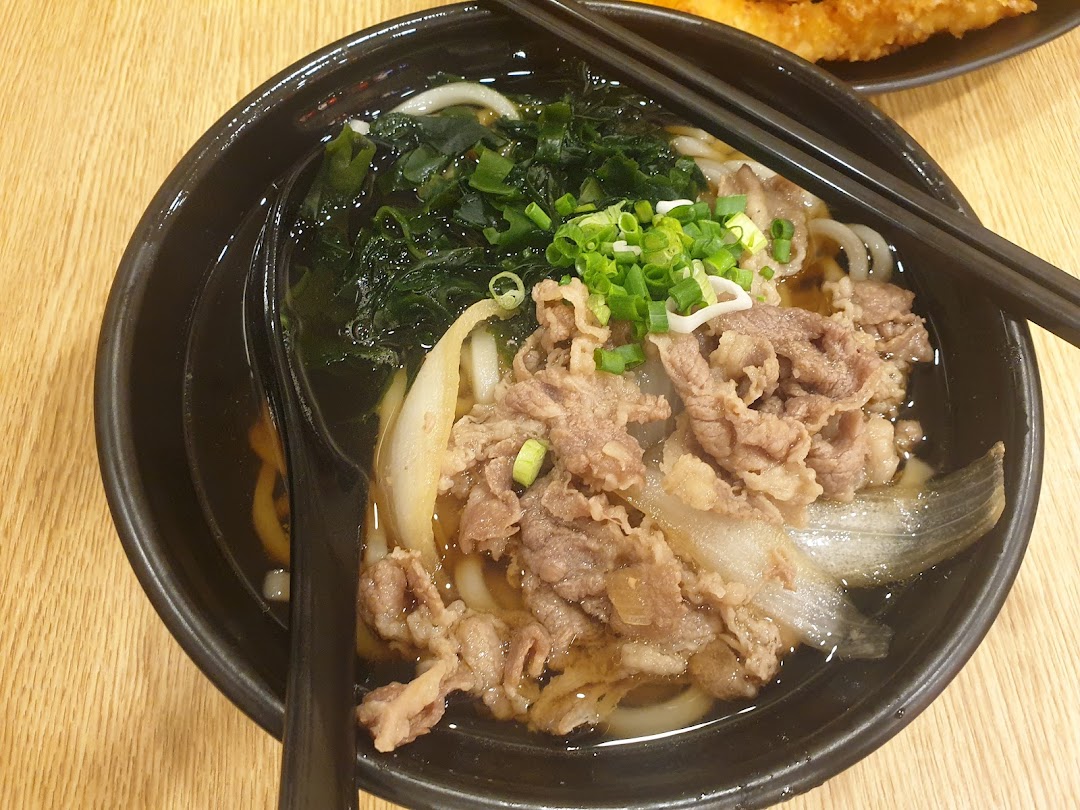 A close-up of a delicious bowl of Japanese udon noodles with beef, seaweed, and green onions.