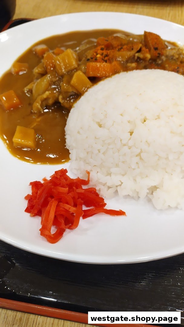 A plate of Japanese curry rice with vegetables and a side of red pickled ginger.