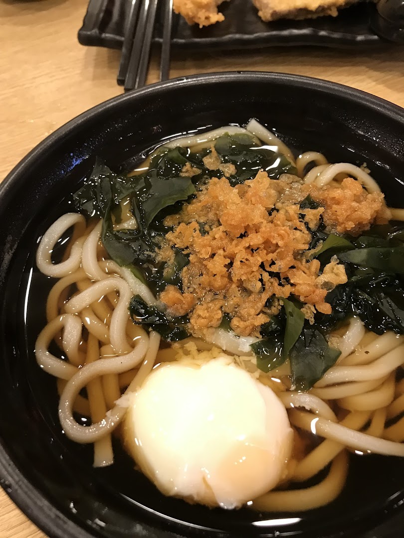A close-up of a delicious bowl of udon noodles with a poached egg, seaweed, and tempura flakes.