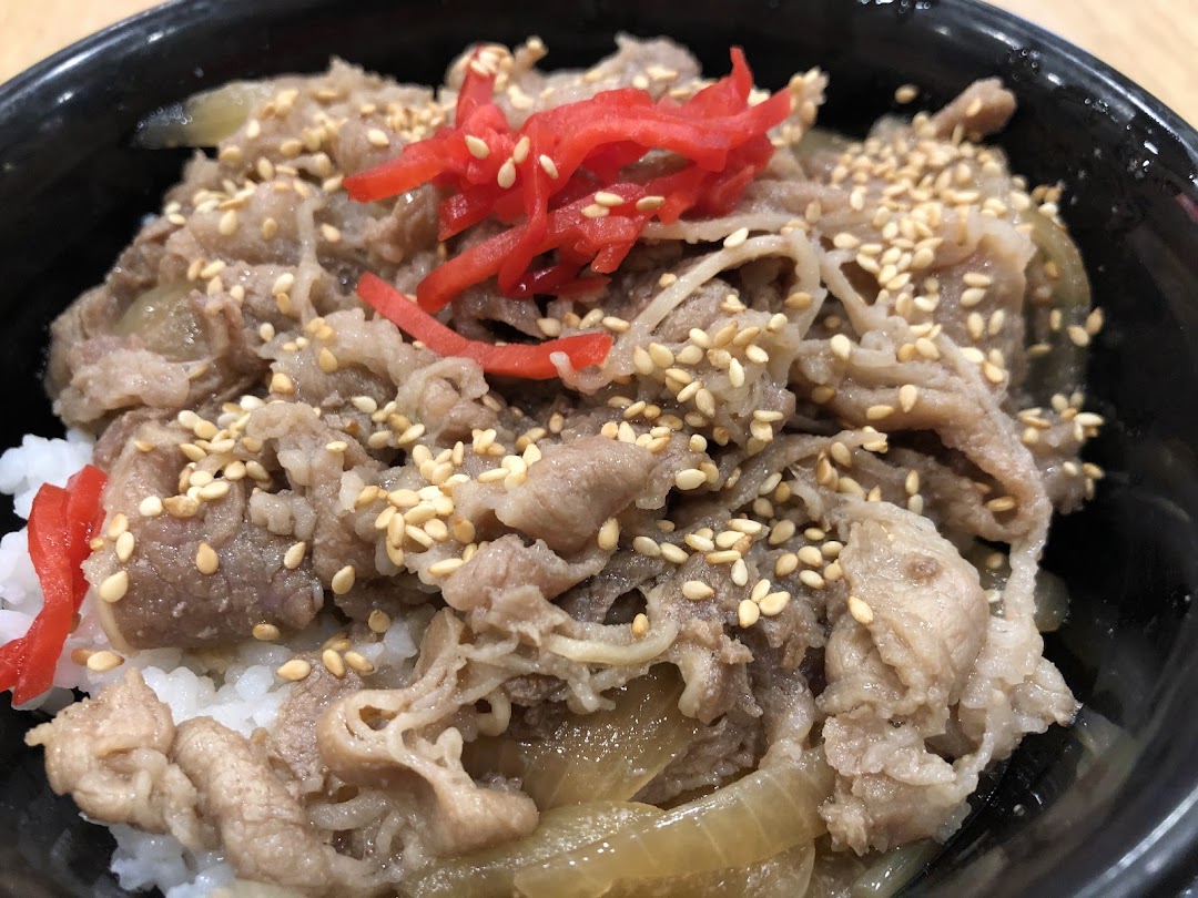 A close-up of a Japanese beef bowl (gyudon) with thinly sliced beef, onions, sesame seeds, and red pickled ginger over rice.
