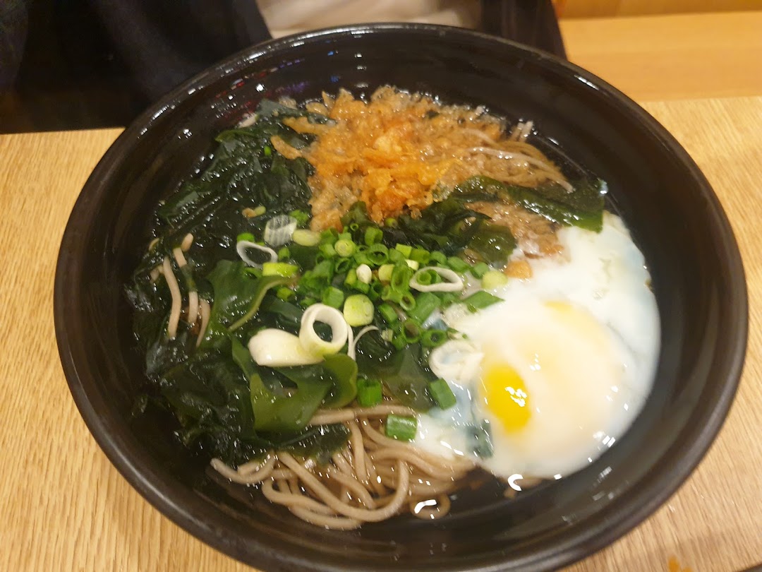 A close-up of a delicious Japanese noodle bowl with seaweed, green onions, tempura flakes, and a poached egg.