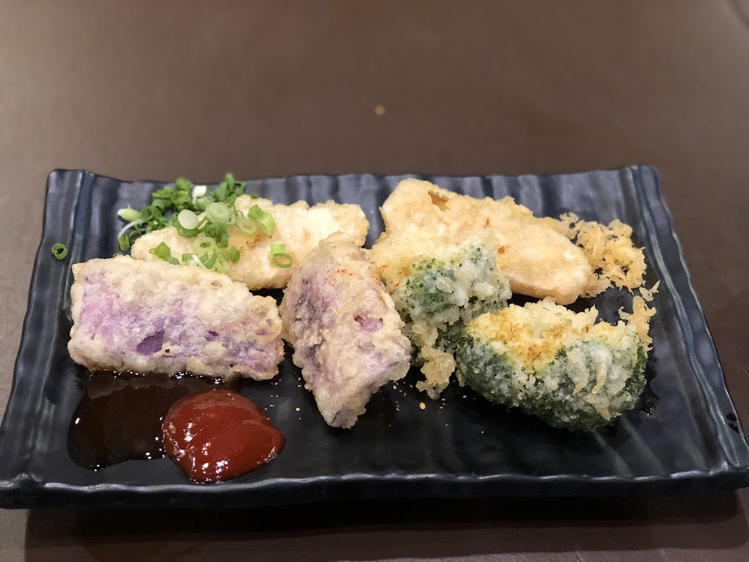 A plate of assorted tempura, including purple sweet potato, fish, and broccoli, served with sauces.