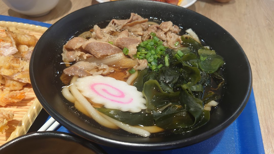 A close-up of a delicious bowl of beef udon with seaweed and fish cake, alongside crispy tempura.