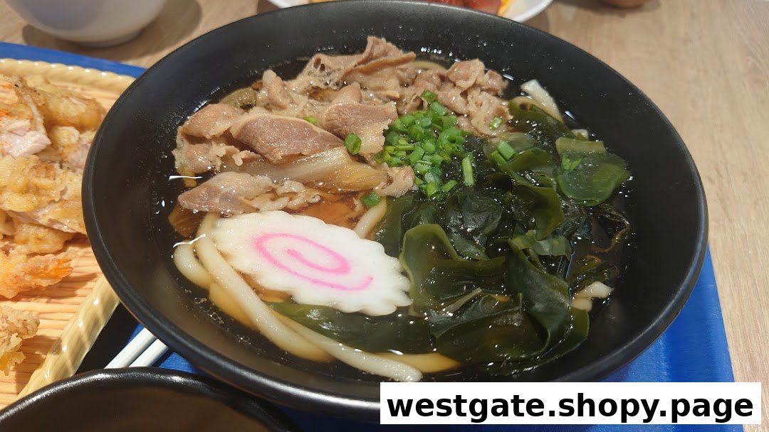 A close-up of a delicious bowl of beef udon with seaweed and fish cake, alongside crispy tempura.