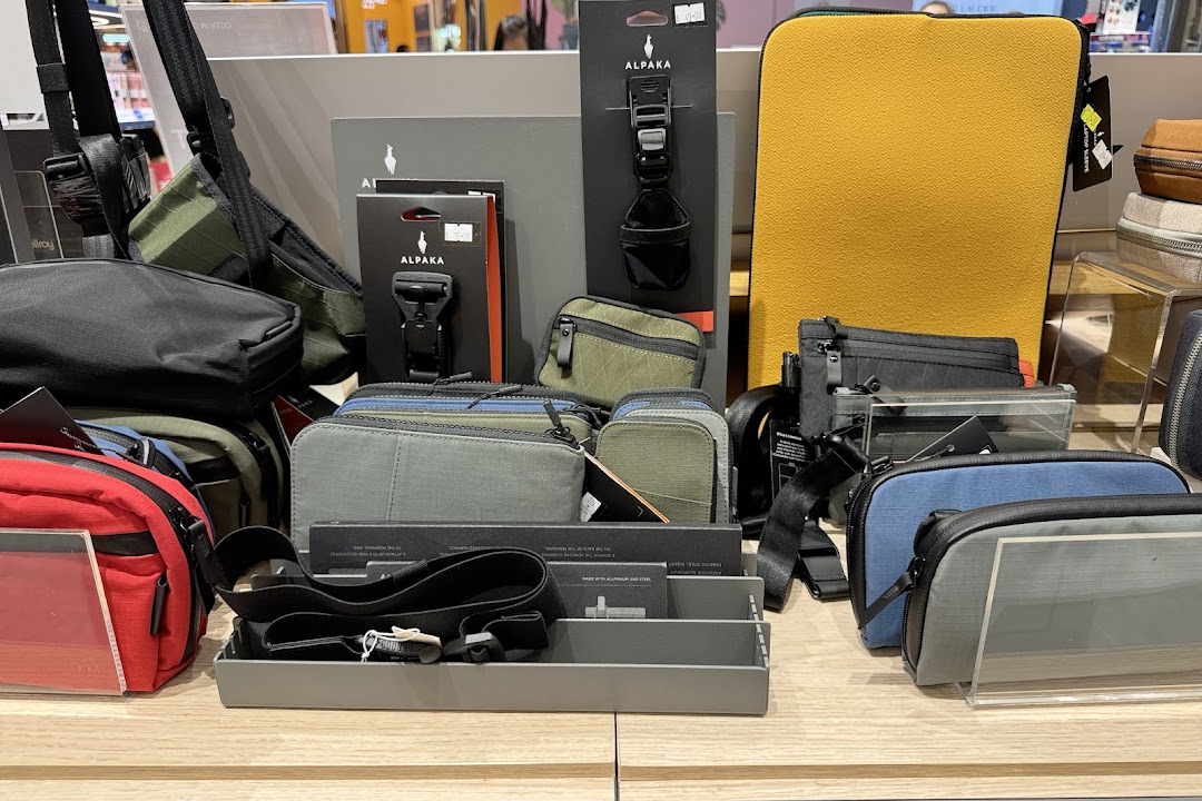 A display of various travel and everyday carry bags, pouches, and accessories, including Alpaka brand items.