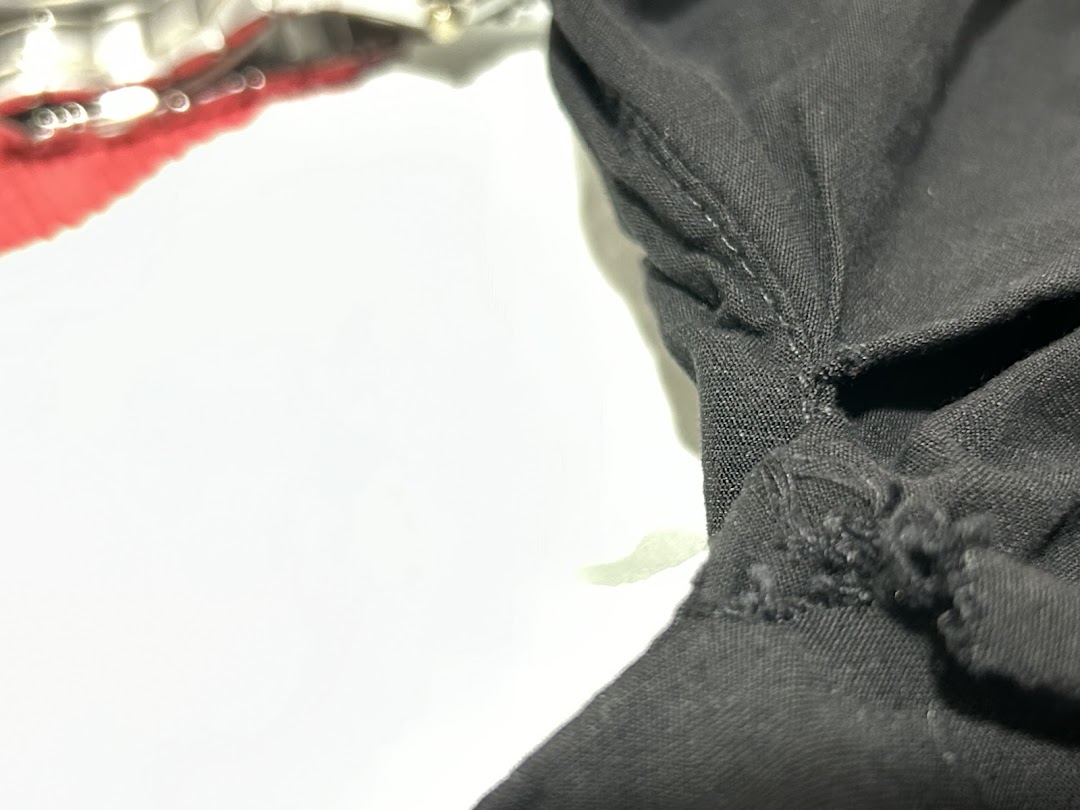 Close-up of black fabric with visible stitching, possibly clothing, against a white background.
