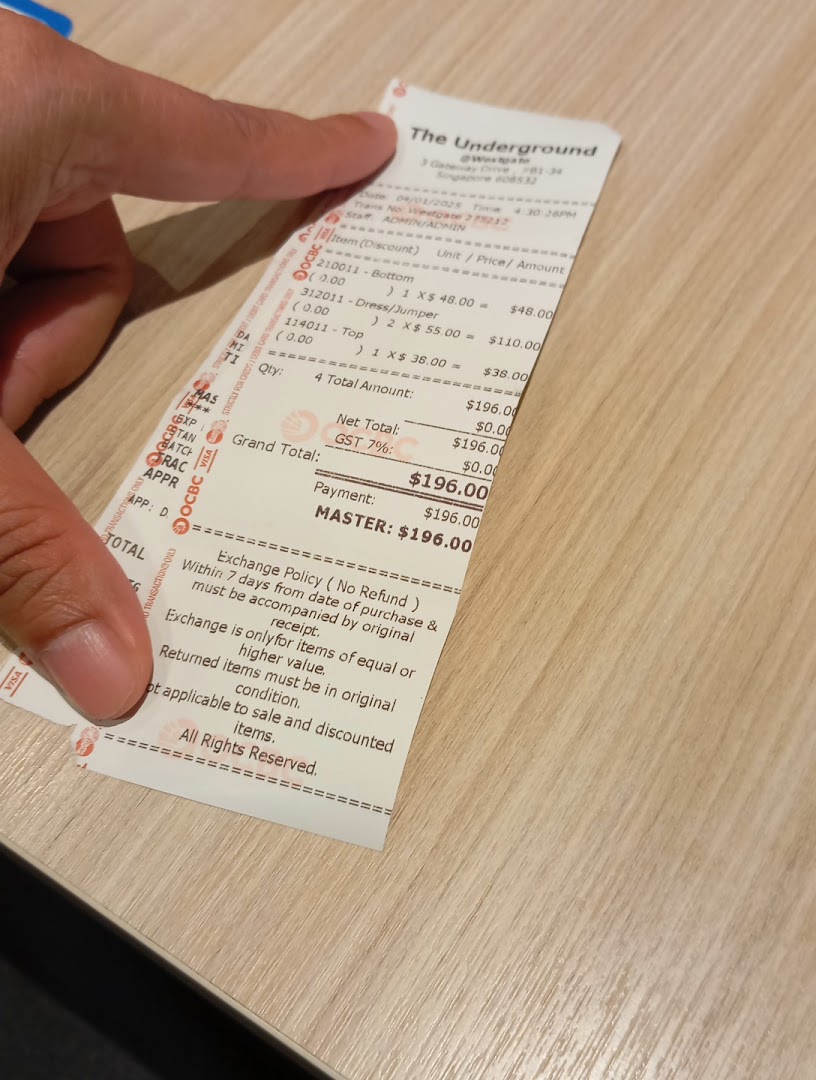 A hand holds a detailed shopping receipt from The Underground, showing clothing purchases.