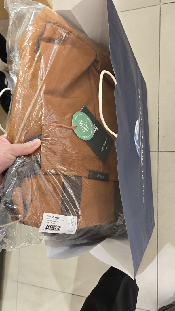 A new brown Tokyo Totepack bag with tags being placed into a shopping bag.