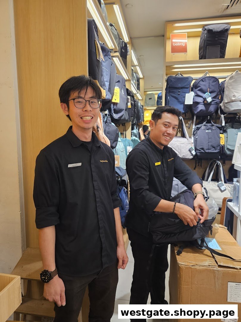 Two smiling staff members in a shop filled with various bags and backpacks on display.