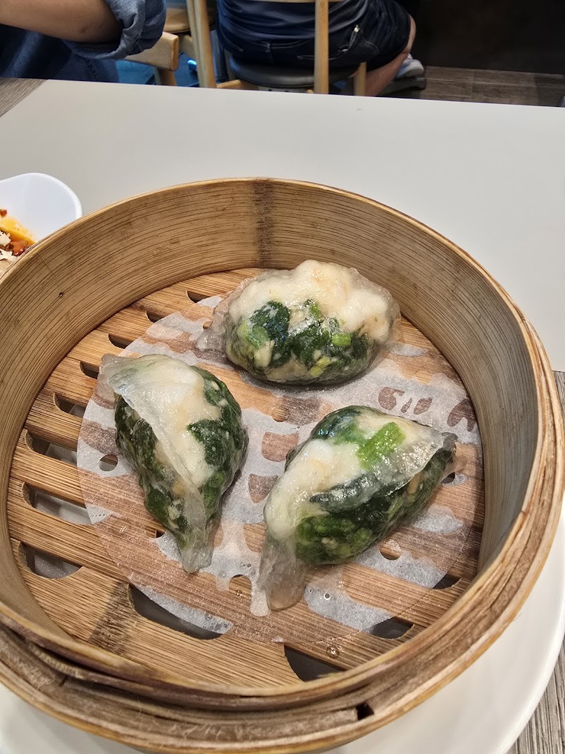Three steamed dumplings with translucent skin and green filling served in a traditional bamboo steamer.