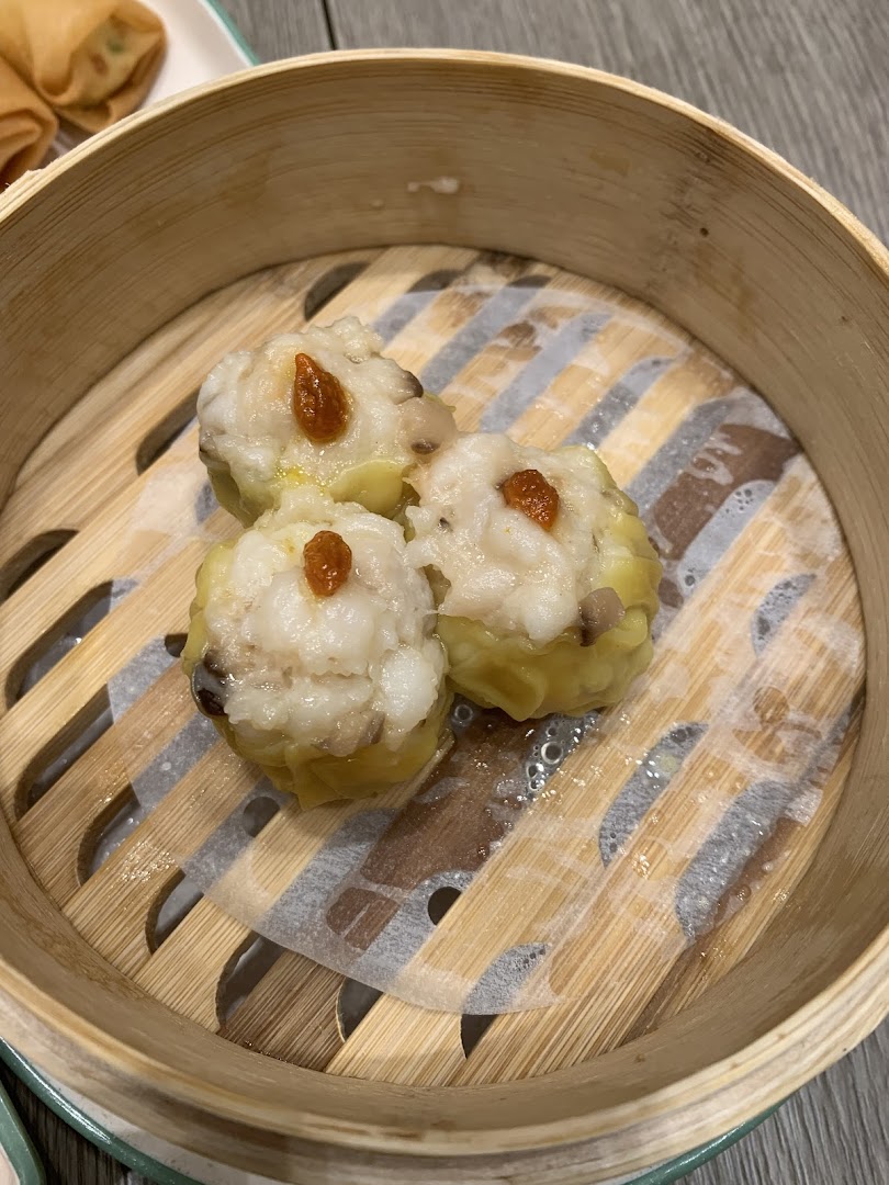 Three delicious dim sum pieces, possibly siew mai, served in a traditional bamboo steamer basket.