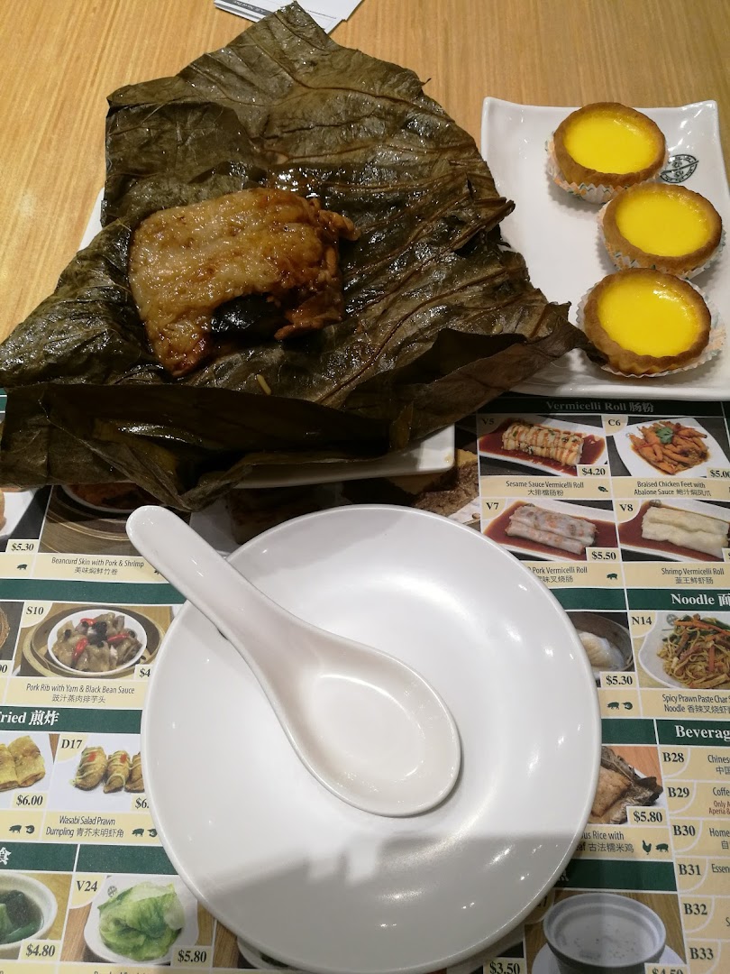 Dim sum dishes, including lotus leaf wrapped glutinous rice and egg tarts, on a table with a partial menu.