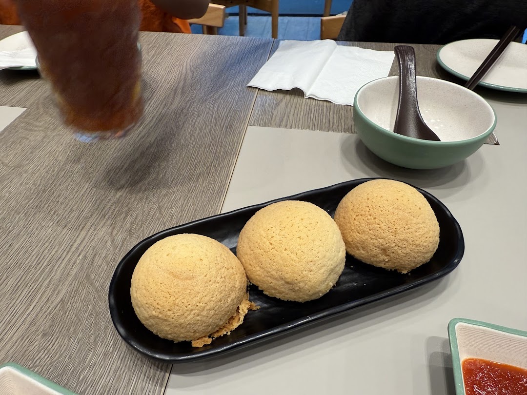Three golden-baked buns on a black plate, with a drink and a bowl on a table.