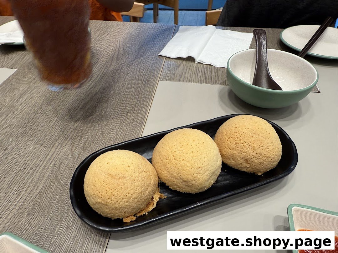 Three golden-baked buns on a black plate, with a drink and a bowl on a table.