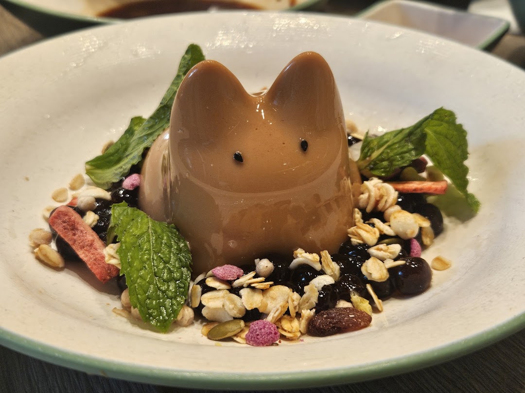 A charming cat-shaped dessert with granola, berries, and mint on a white plate.