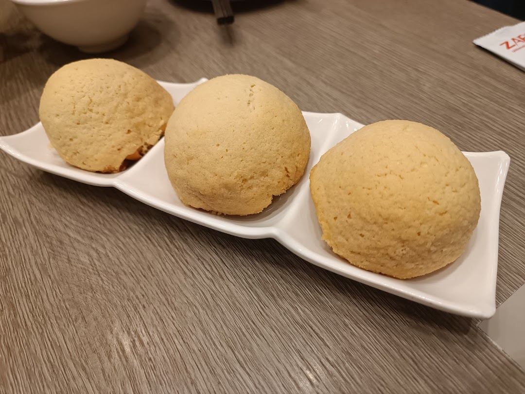 Three golden-baked buns, likely Tim Ho Wan's famous BBQ pork buns, served on a white plate.